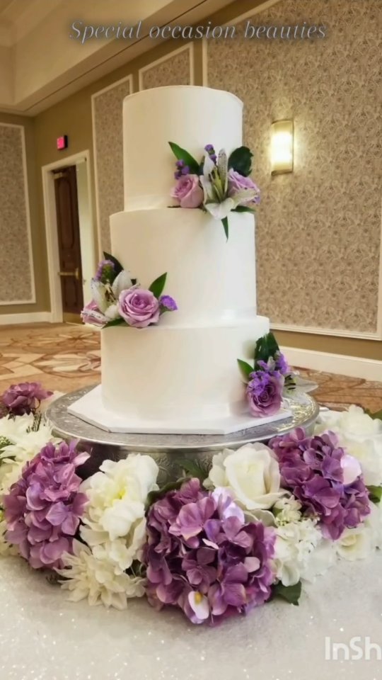 White tiered wedding cake with a purple and white flower arrangement